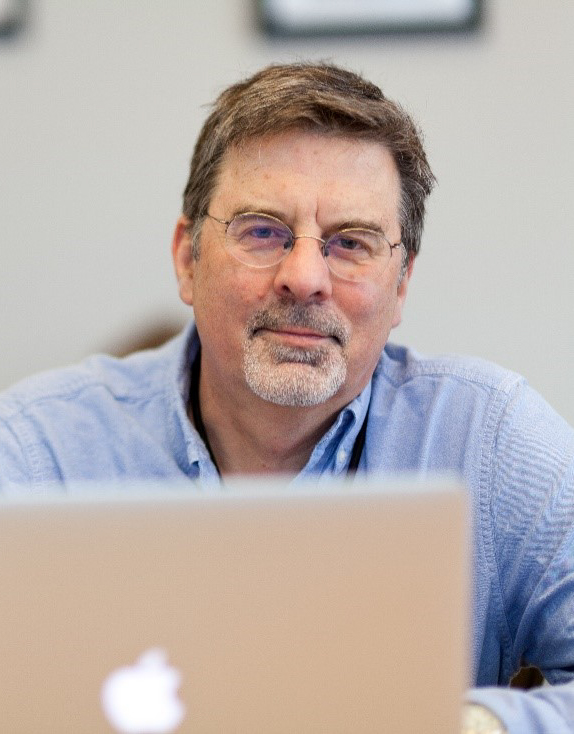 Doctor Andreas Laupacis with glasses and a light blue shirt sits at a table, working on a laptop in a casual indoor setting.