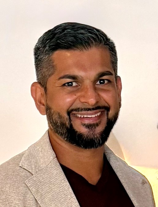 Doctor Kang with short dark hair and beard, wearing a beige blazer and maroon shirt, smiling in front of a plain background.