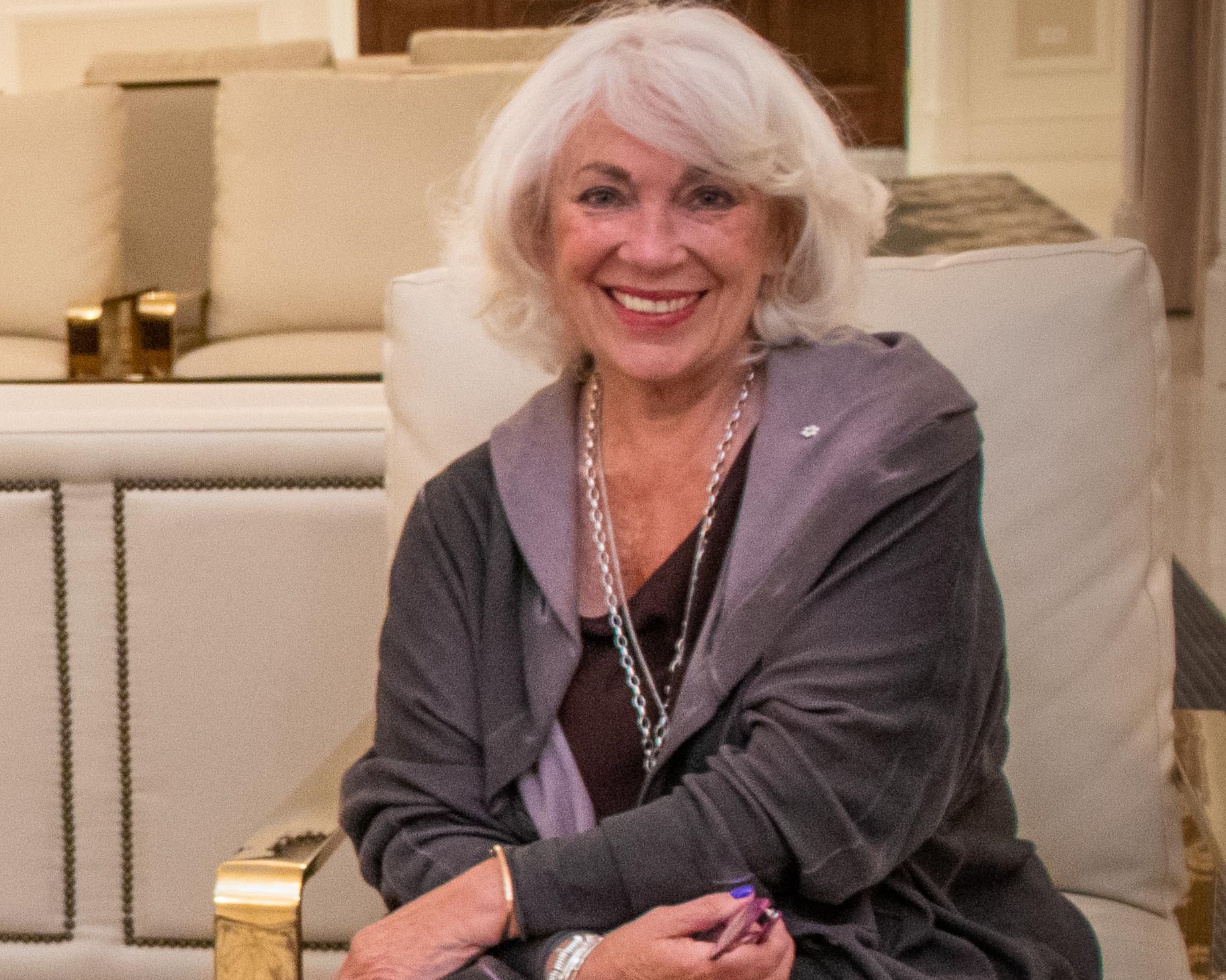 Janet sits smiling on a cream-colored armchair in a modern room.