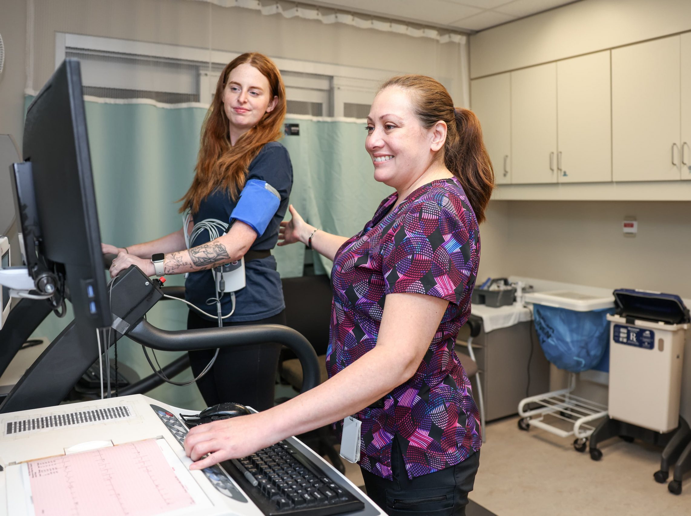 A healthcare worker monitors a patient on a treadmill during a medical test in a clinical setting.