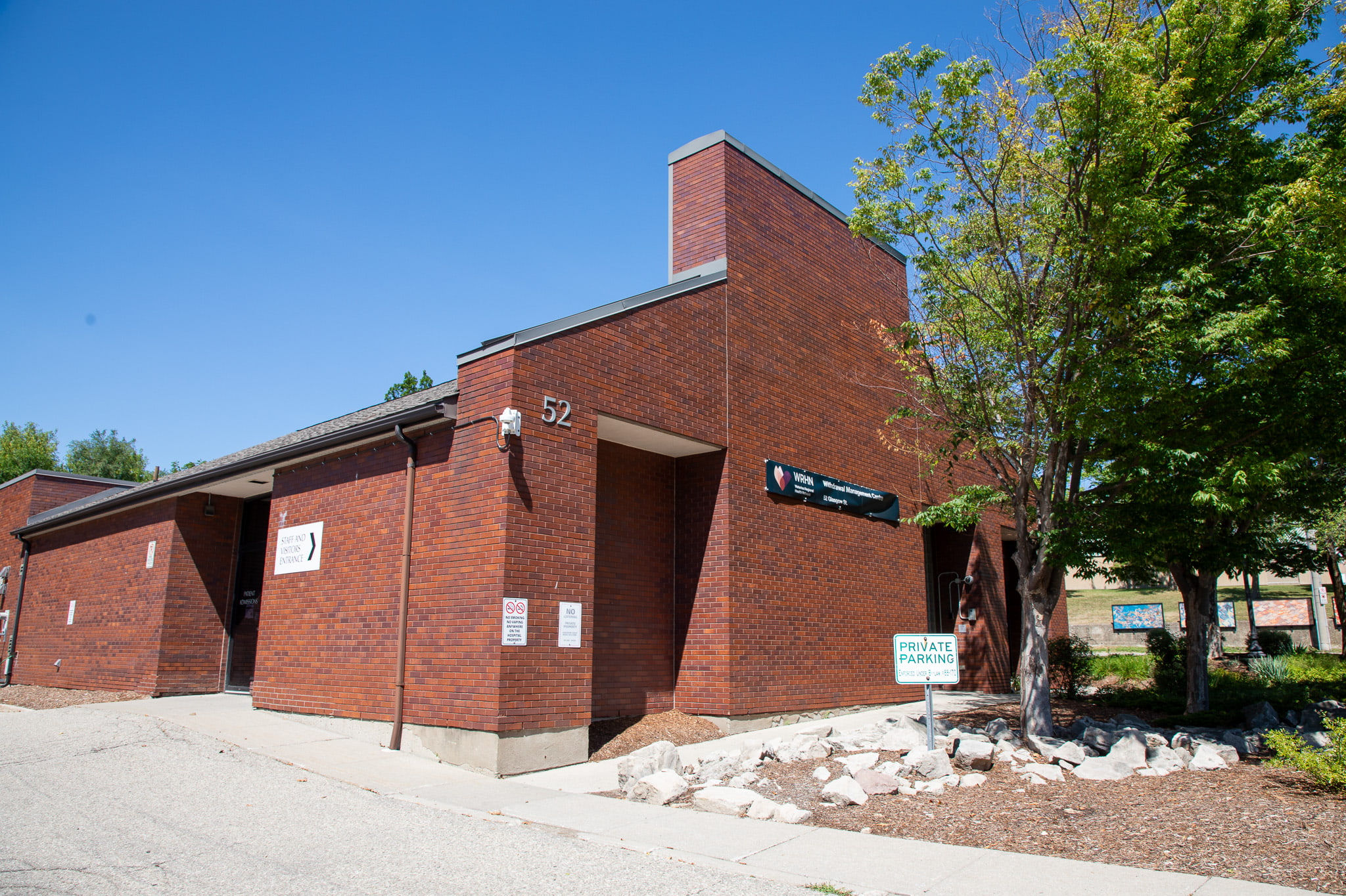 A red brick building with the number 52, private parking sign, and a tree on the right side, under a clear blue sky.