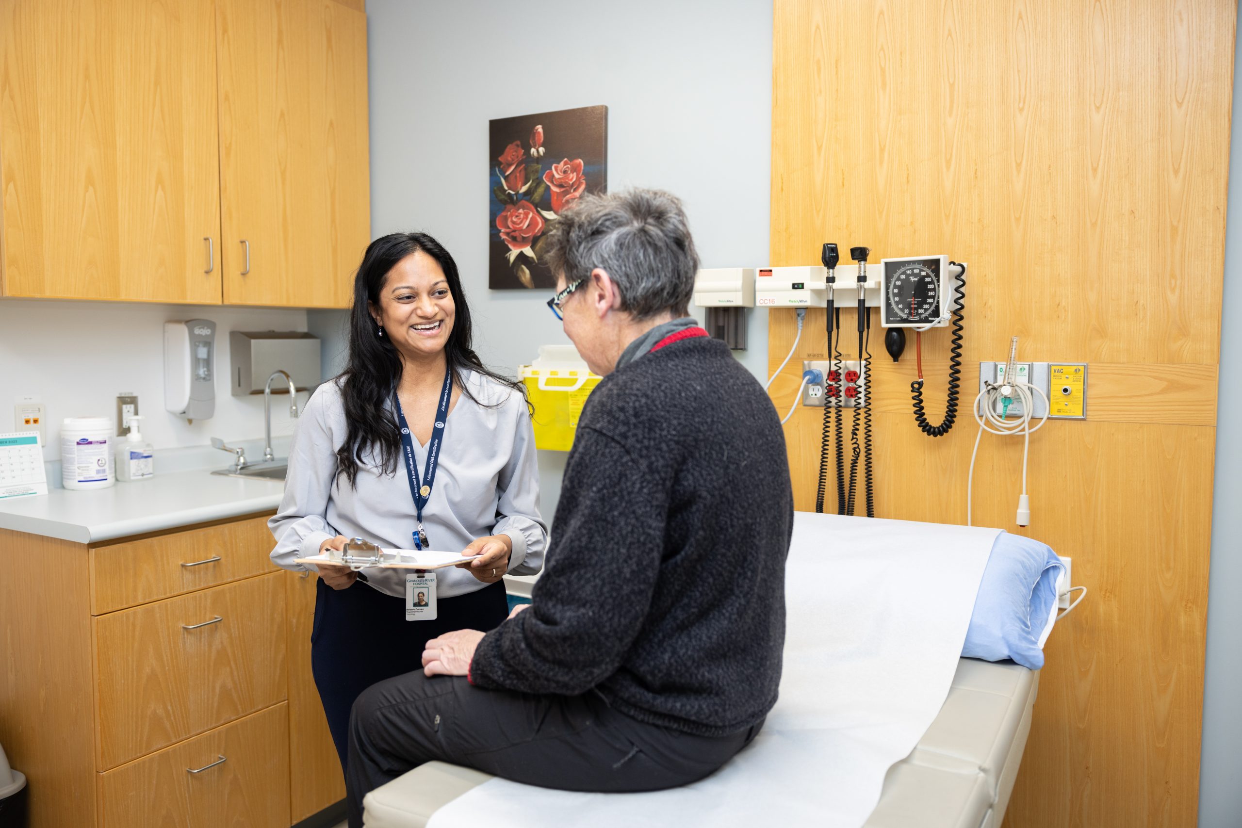 A healthcare professional talks with a patient sitting on an exam table in a medical office.