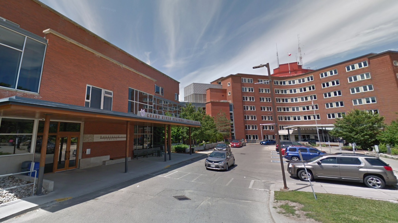 一座砖砌的医院建筑，入口处有遮阳棚，停放着车辆，头顶是多云的天空。