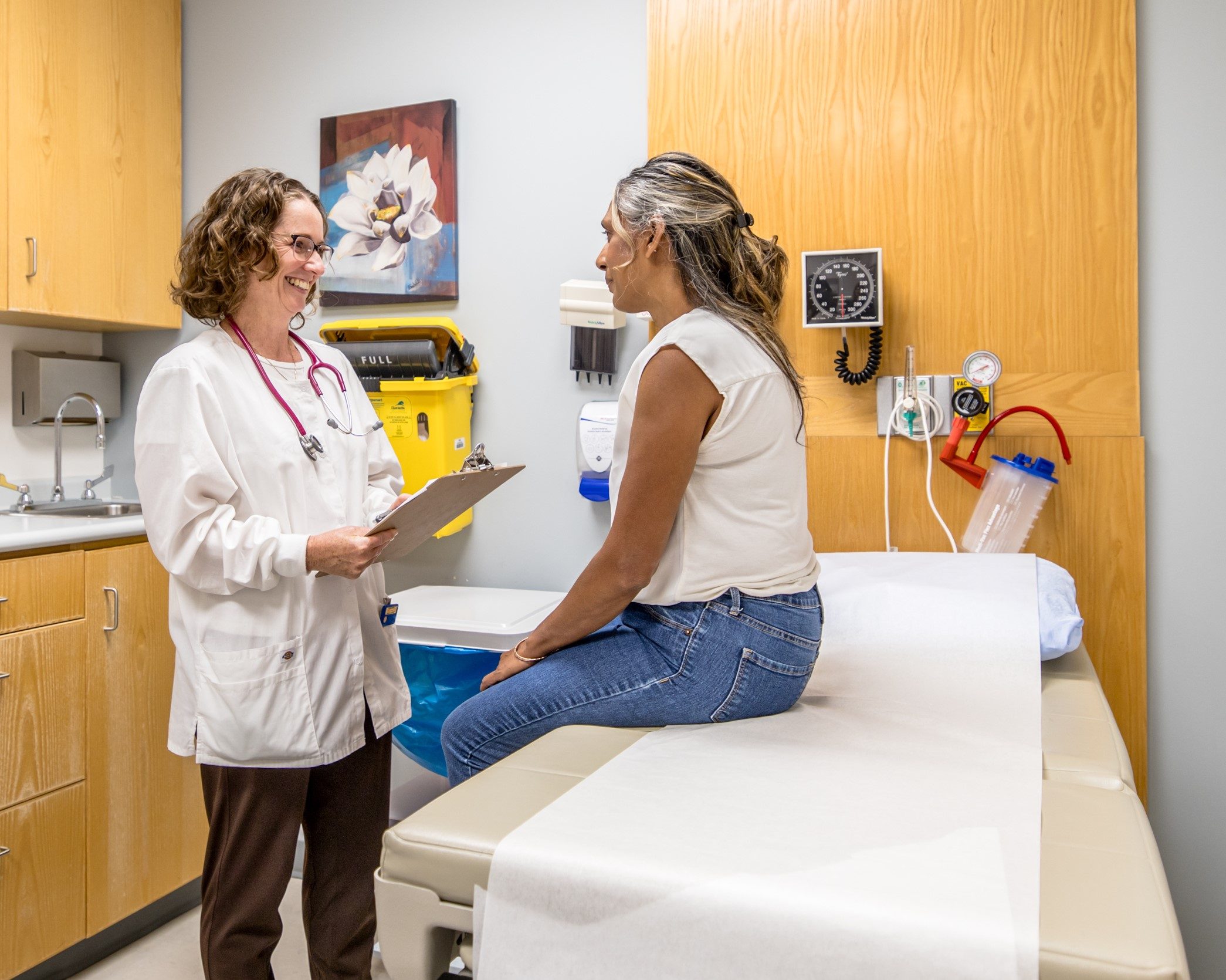 A healthcare provider talks with a patient sitting on an exam table in a medical examination room.